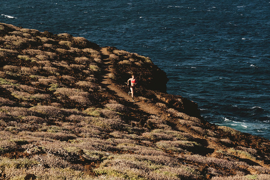 Sunset Photograph - Pulled Back View Of Woman Running On Trail By The Sea by Cavan Images