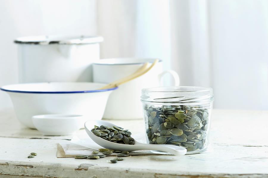 Pumpkin Seeds In A Glass Jar And On A Spoon On A Rustic Kitchen Table Photograph by Achim Sass
