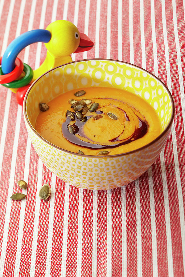 Pumpkin Soup With Oil And Seeds In A Bowl Next To A Baby Rattle Photograph by Meike Bergmann