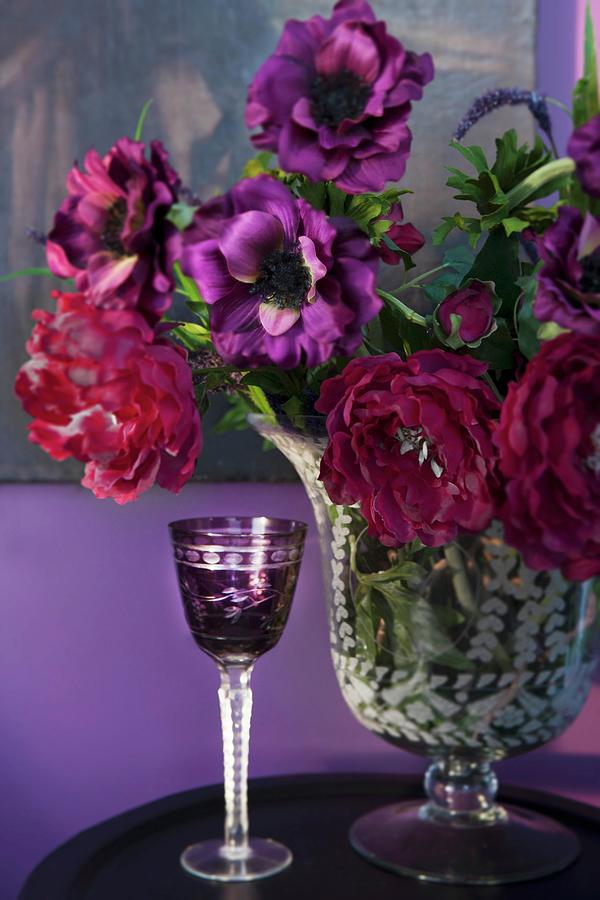 Purple, Crystal Liqueur Glass Next To Vase Of Flowers In Various Shades Of Red Photograph by Annette Nordstrom