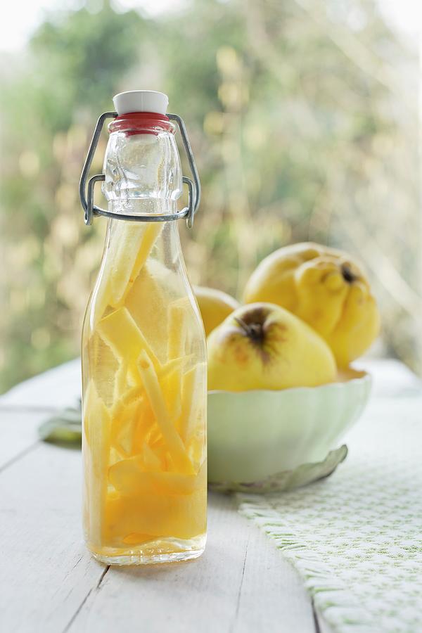 Quince Schnapps In A Bottle, With Fresh Quinces In A Vintage Bowl In The Background Photograph by Sabine Lscher
