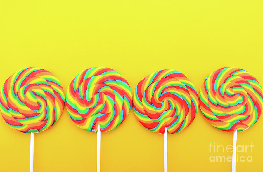 Candy Photograph - Rainbow lollipop candy on bright yellow wood table.  by Milleflore Images