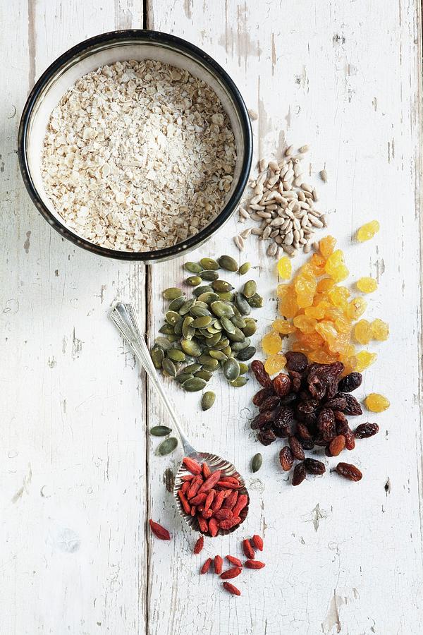 Raisins, Golden Raisins, Pumpkin Seeds, Sunflower Seeds And Goji Berries In Small Piles, And A Bowl Of Oats Photograph by Victoria Firmston
