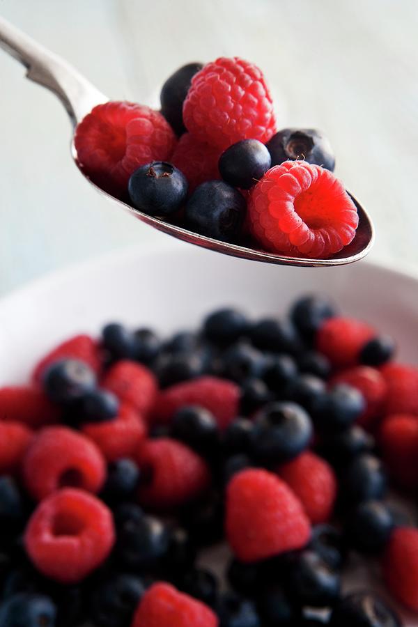 Raspberries And Blueberries On A Spoon And In A Bowl Photograph by Stowell, Roger