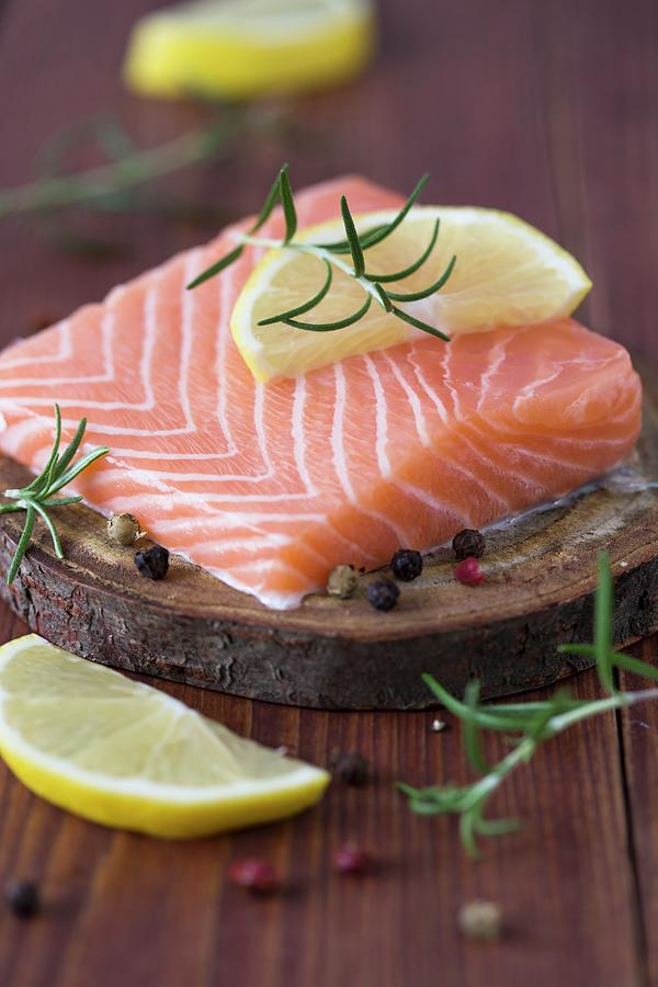 Raw Salmon Fillet With Lemon, Rosemary And Pepper On A Slice Of Bark Photograph by Malgorzata Laniak