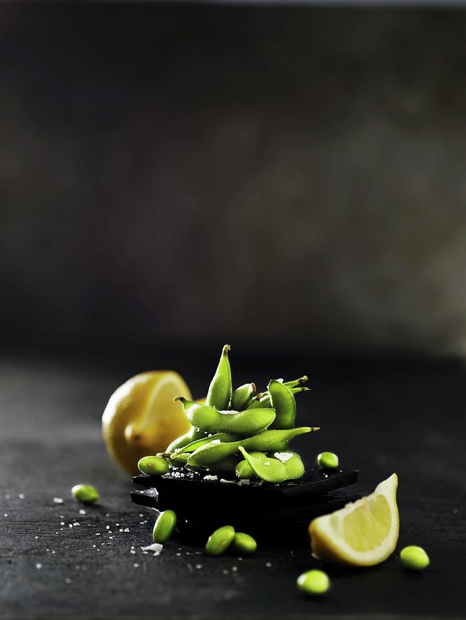 Raw Soya Beans With Pods On A Black Slate Platter With A Sliced Lemon Photograph by Mikkel Adsbl