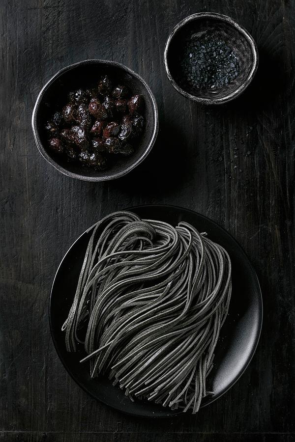 Raw Uncooked Black Cuttlefish Ink Spaghetti Pasta With Black Olives And Black Salt Over Black Background View From Above Photograph by Natasha Breen