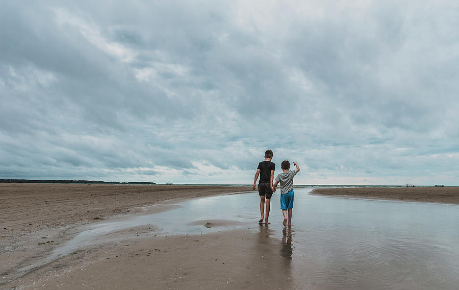 Nature Photograph - Rear View Of Brothers Holding Hands While Walking At Beach Against Cloudy Sky by Cavan Images