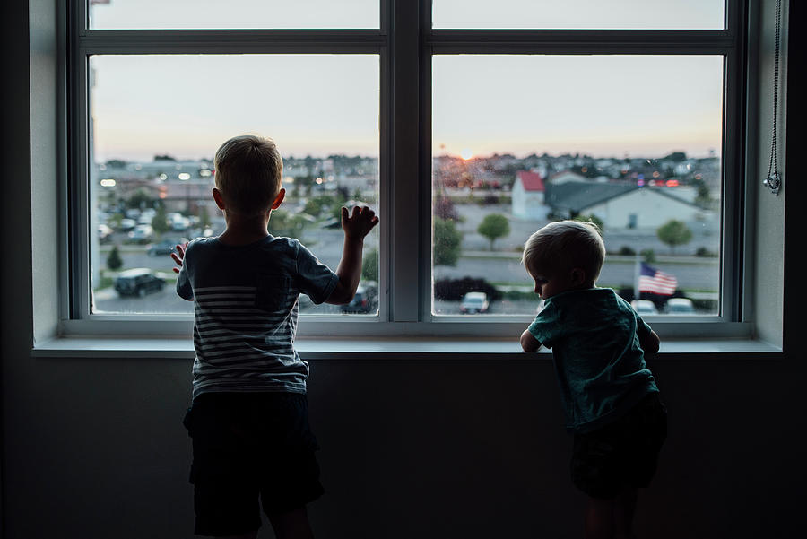 Sunset Photograph - Rear View Of Brothers Looking Through Window While Standing At Home During Sunset by Cavan Images