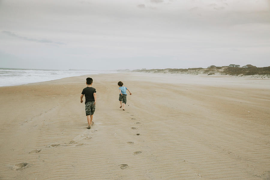 Nature Photograph - Rear View Of Brothers Walking On Sand At Beach Against Cloudy Sky by Cavan Images