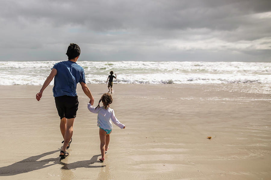 Rear View Of Father And Daughter Holding Hands While Son Running ...