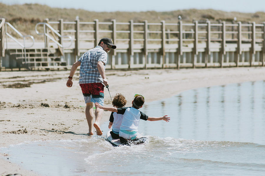 Rear View Of Happy Father Pulling Sons Sitting On Surfboard In Sea ...