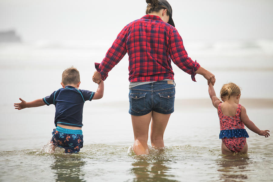 Nature Photograph - Rear View Of Mother Helping Kids Wade Through Water At The Beach. by Cavan Images