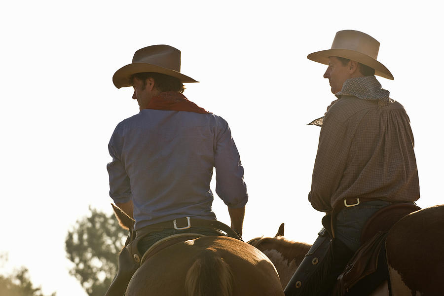 Rear View Of Two Cowboys Riding Horses Photograph by Adam Burn