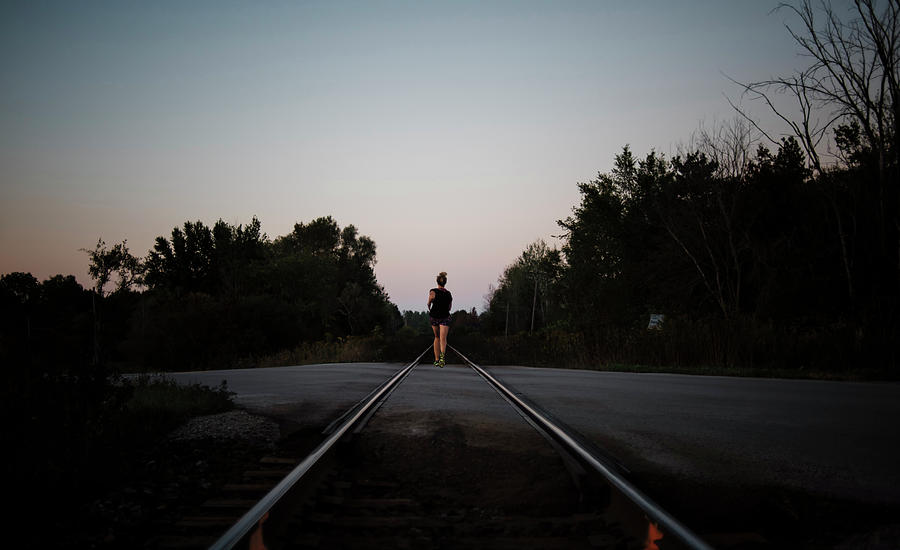 Nature Photograph - Rear View Of Woman Jogging On Railroad Track Against Clear Sky During Dusk by Cavan Images