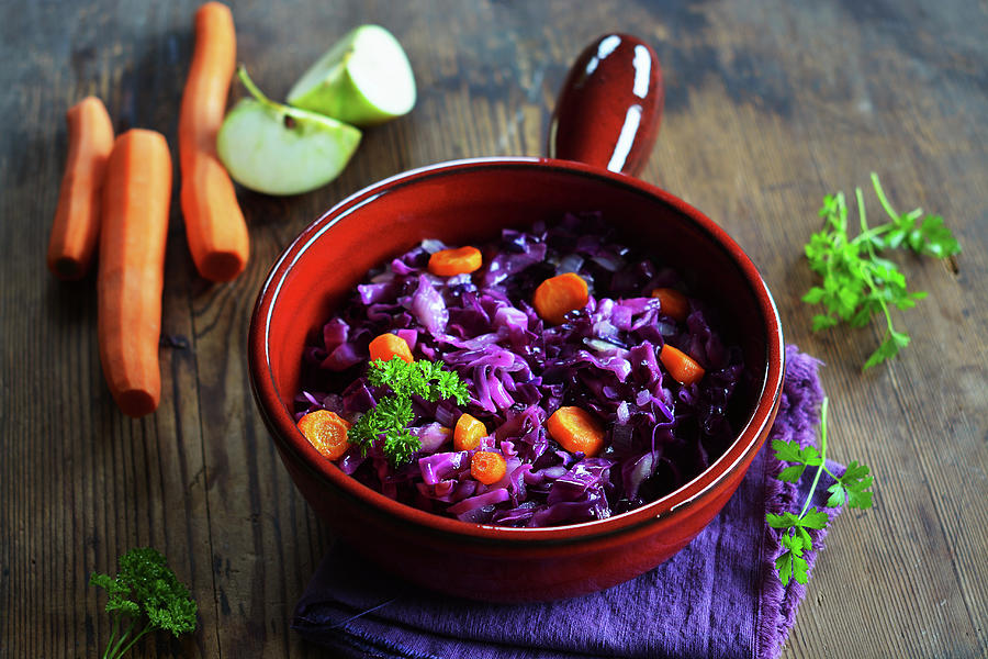 Red Cabbage With Carrots And Apple In A Ceramic Pot With Fresh Ingredients In The Background Photograph by Mariola Streim