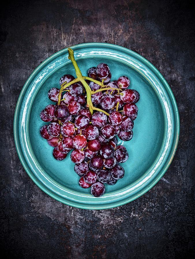 Red Grapes On A Blue Plate Against A Grey Background Photograph by Peter Rees