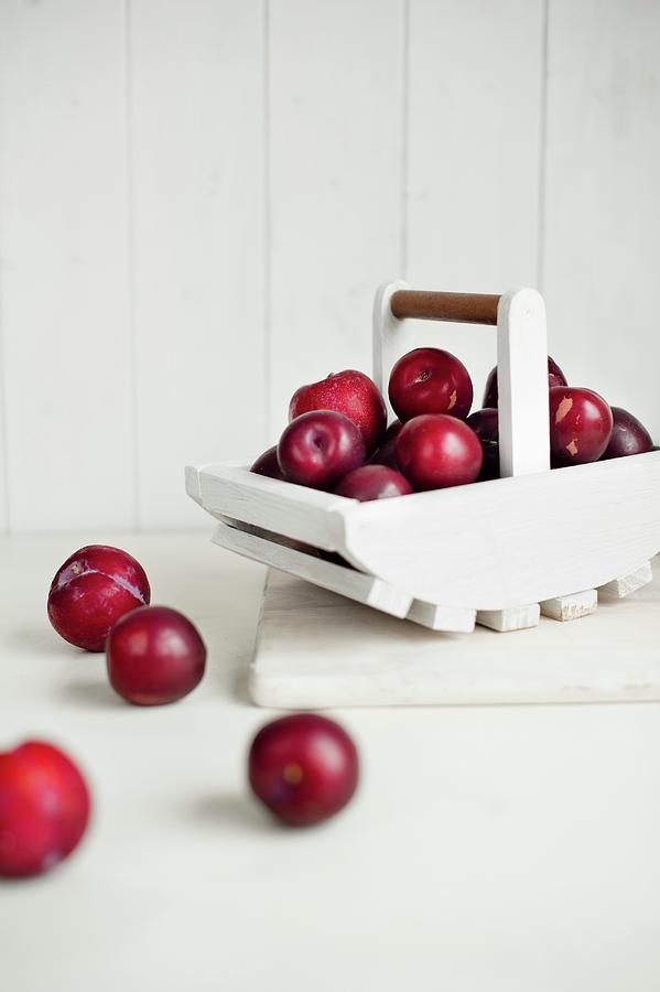 Red Plums In White Wooden Basket And In Front Of It Photograph by Magdalena Hendey