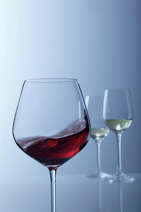 Red Wine Swirling In A Glass With Two Glasses Of White Wine In The Background Photograph by Jalag / Gtz Wrage