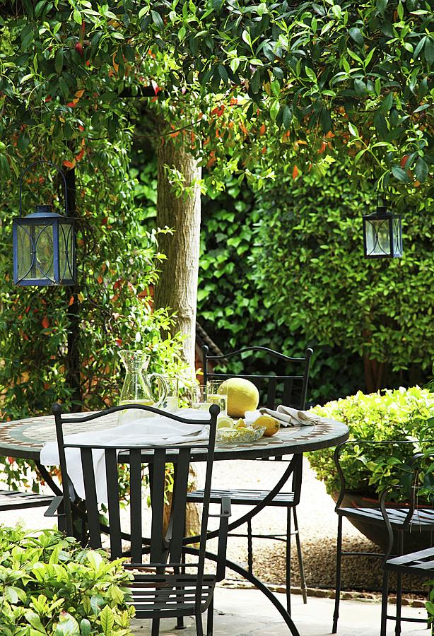 Refreshing Drinks On Metal Garden Table With Matching Chairs And Lanterns Hanging From Tree In Sunny Garden Photograph by Jos-luis Hausmann