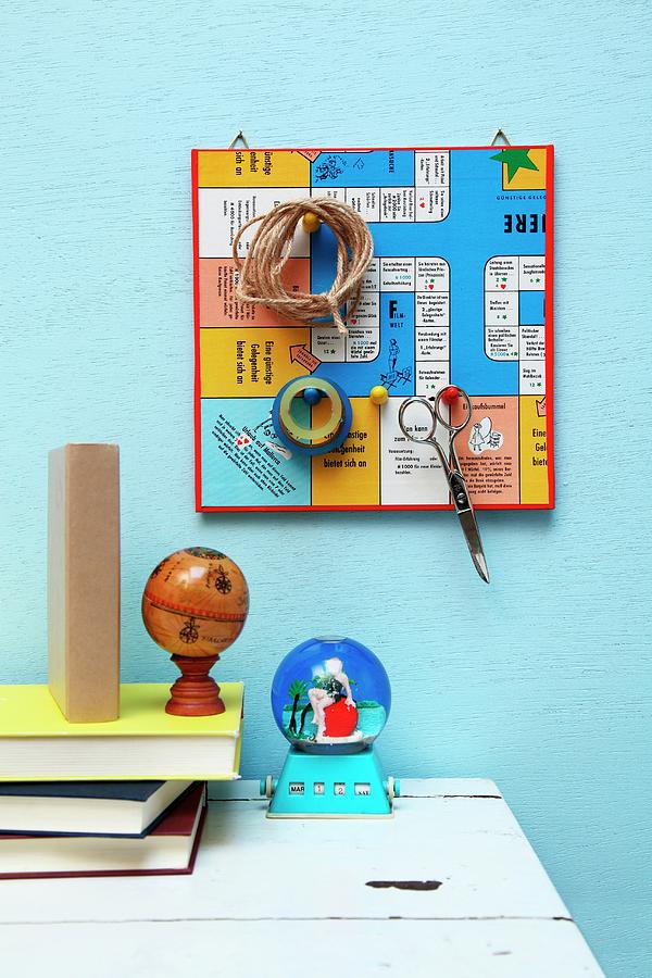 Retro Board Game Used As Pin Board With Gaming Pieces Used As Hooks For Scissors, Twine And Sticky Tape Above Stacked Books On Desk Photograph by Thordis Rggeberg
