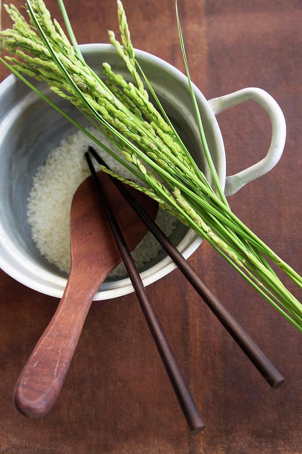 Rice And Ears Of Rice, A Wooden Spoon And Chopsticks In A Pan Of Rice Photograph by Martina Schindler