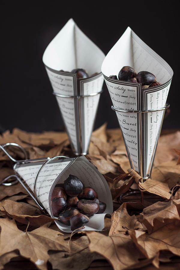 Roast Chestnuts In Paper Cones On Autumn Leaves Photograph by Vernica Orti