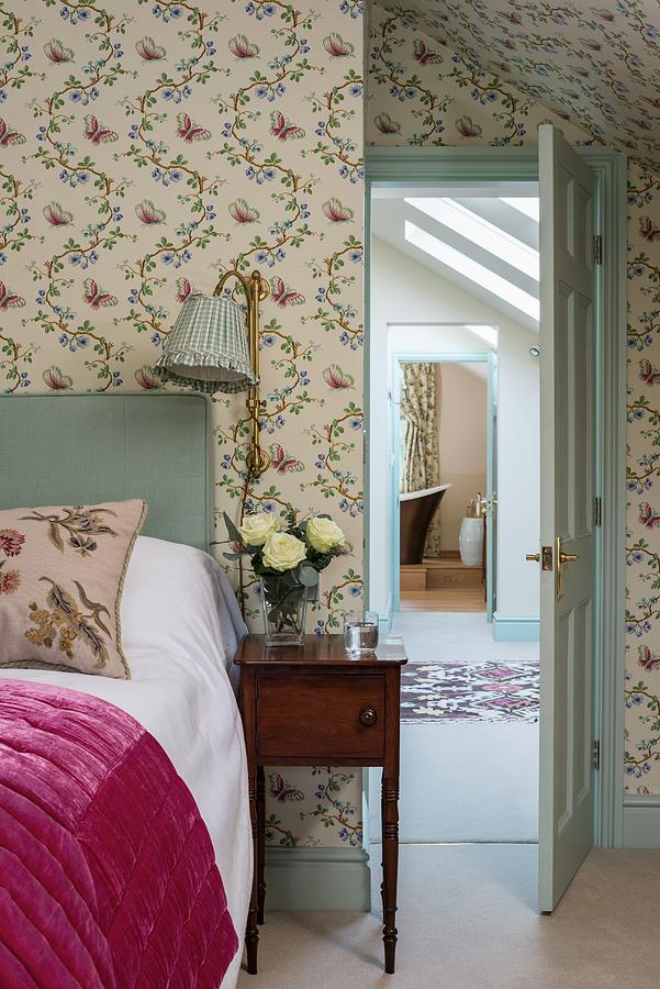 Romantic Bedroom With Floral Wallpaper, Antique Bedside Table And View Through Open Door Photograph by Brian Harrison