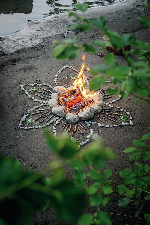 Romantic Campfire On River Bank Surrounded By Flower Pattern Of Stones And Sticks Photograph by Patsy&christian