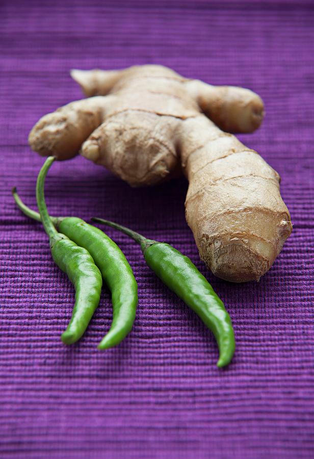 Root Ginger And Green Chilli Peppers On A Purple Surface Photograph by Richard Church