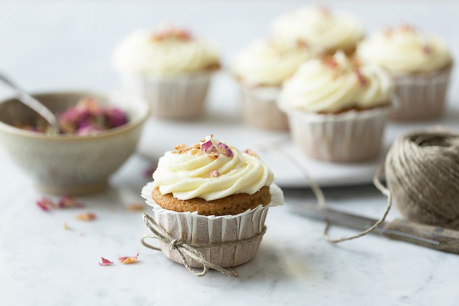 Rose And Lemon Cupcakes With Rosewater And Lemon Frosting Tied With String With Spoon And Bowl Of Rose Petals On A White And Grey Marble Surface Photograph by Sarah Coghill