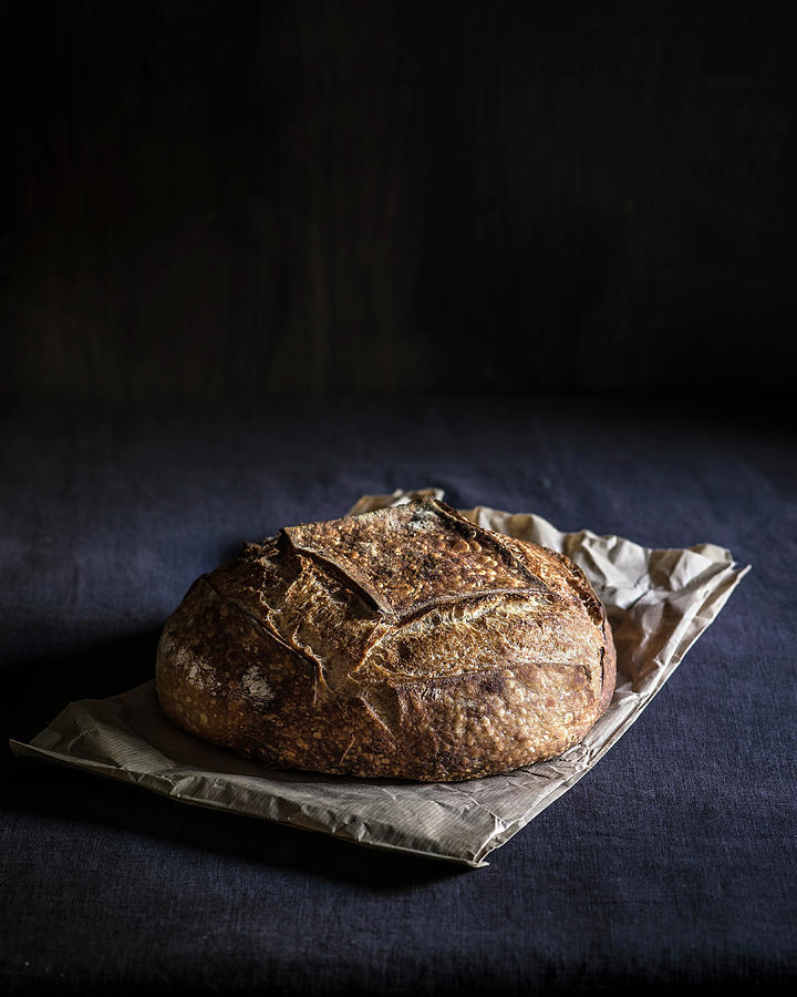 Round Bread Loaf On Paper Bag And Dark Fabric Background Photograph by Miriam Garcia