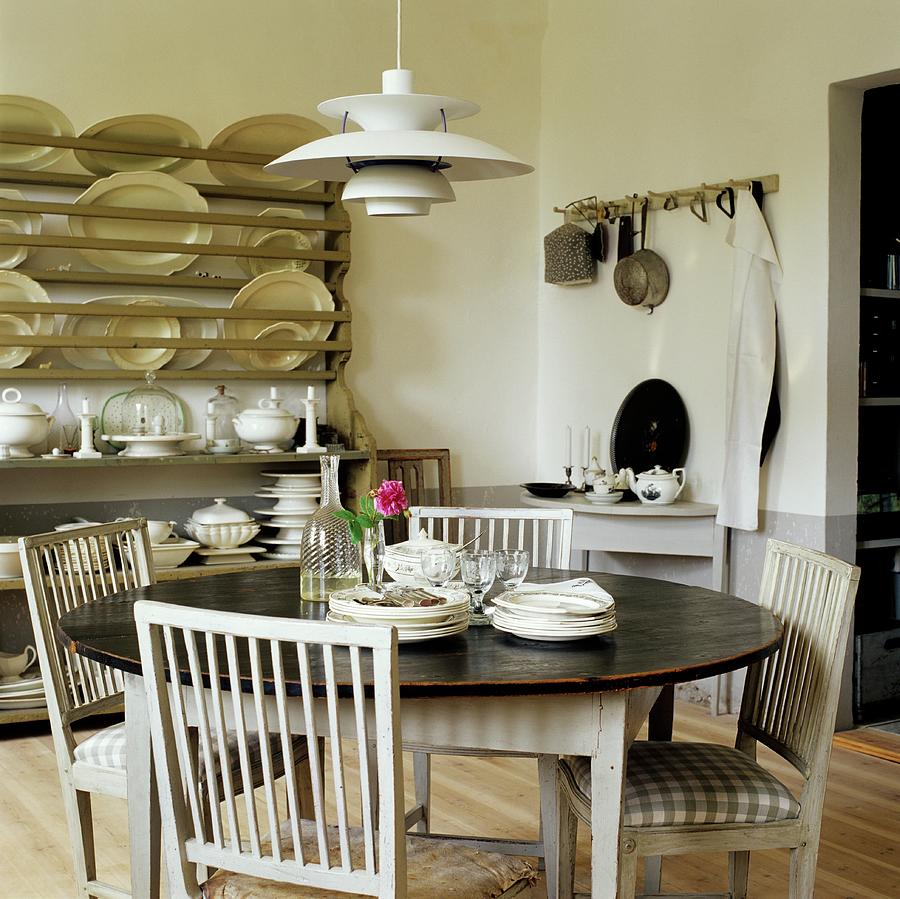 Round Dining Table, Kitchen Chairs With Seat Cushions And 50s, Danish Designer Lamp; Plate Rack In Background Photograph by Tine Guth Linse