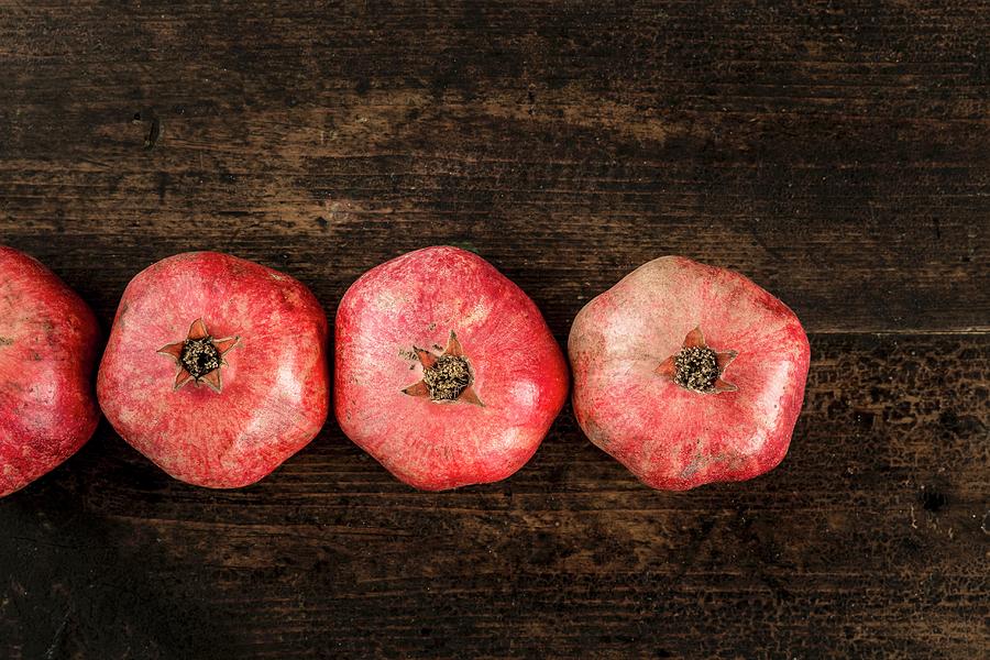 Row Of Pomegranates On A Wooden Surface Photograph by Sarah Coghill
