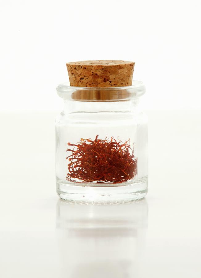 Saffron Threads In A Glass Bottle With A Cork On A White Surface Photograph by William Boch