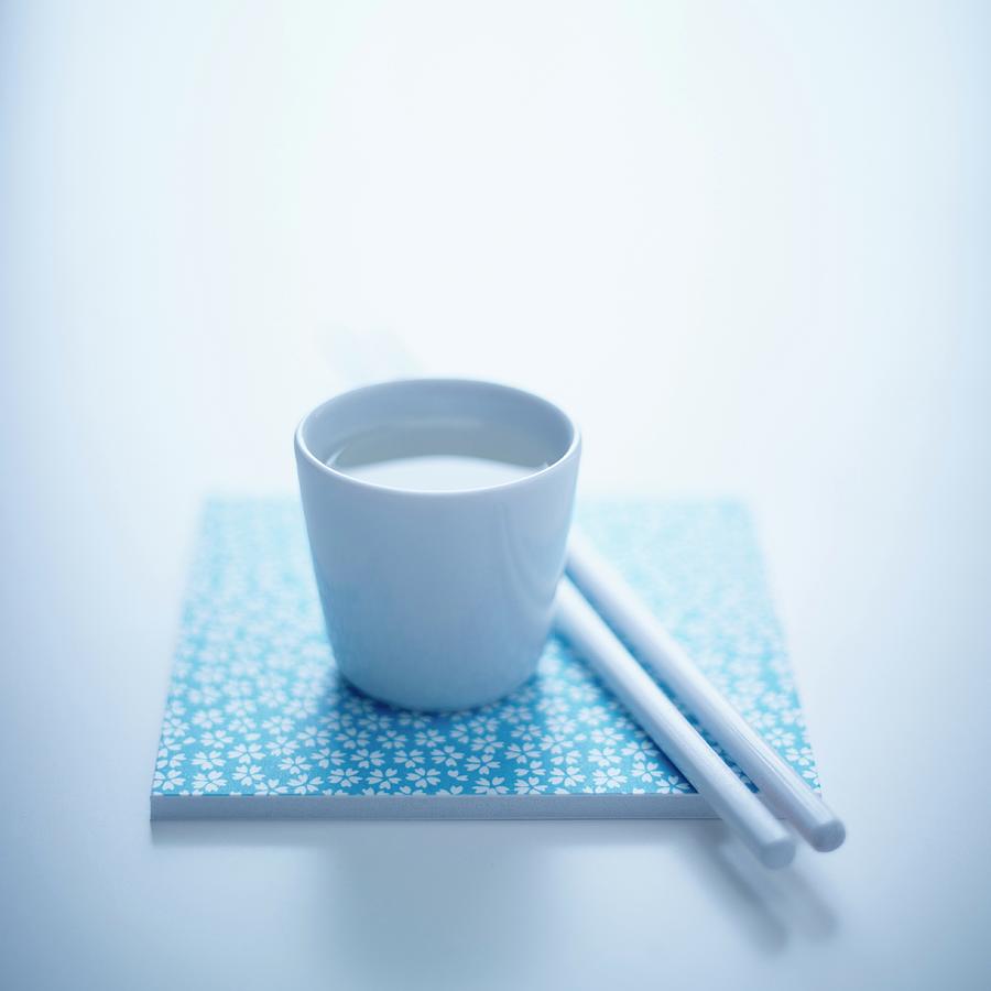 Sake In A Cup Next To A Pair Of Chopsticks Photograph by Will Shaddock Photography