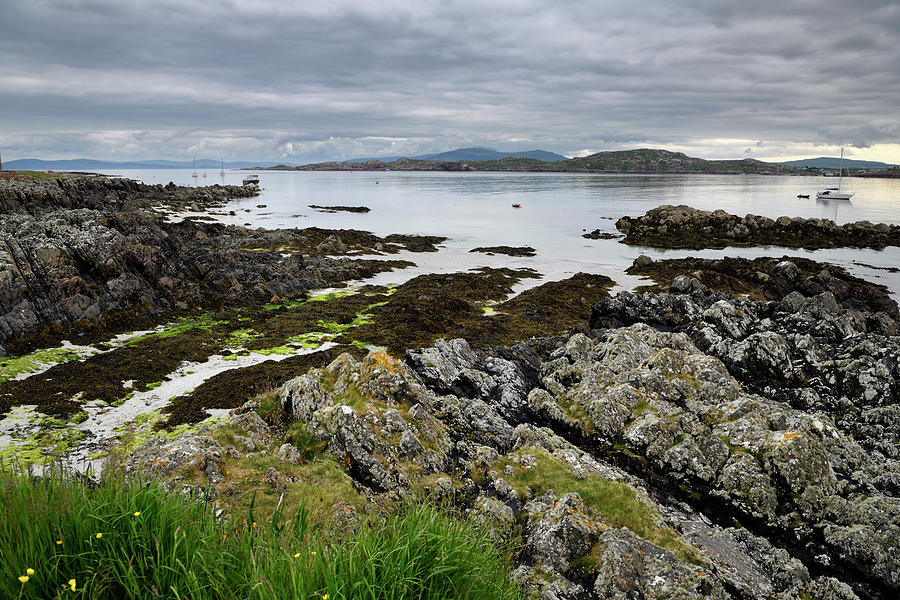 Sand beach and rocky shore under clouds on Isle of Iona with boa Photograph by Reimar Gaertner