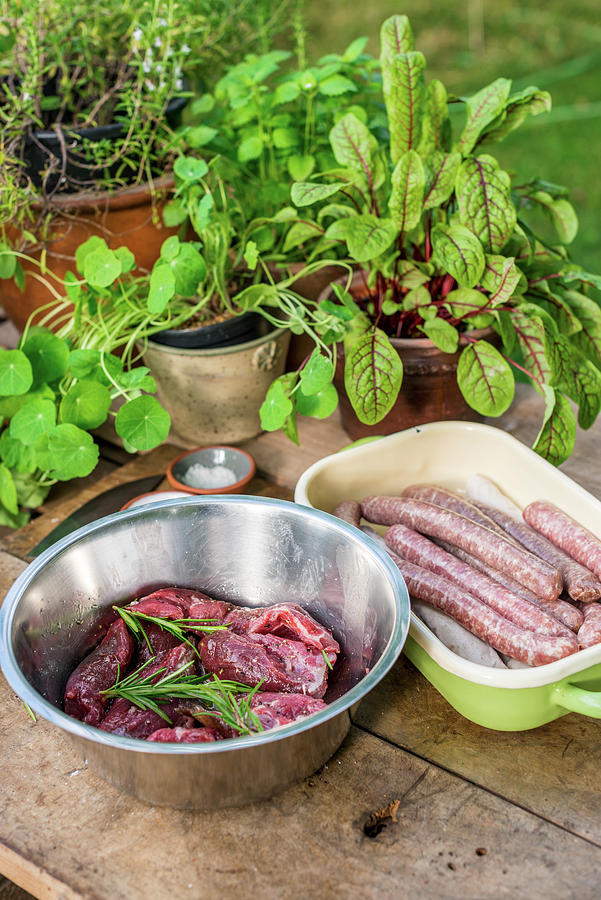 Sausages And Marinated Meat For Grilling On A Wooden Board In A Garden Kitchen Photograph by Sebastian Schollmeyer