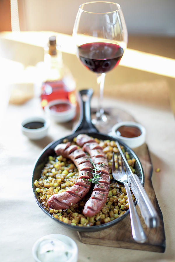 Sausages With Potatoes In A Cast Iron Pan, Table Served With Glass Of Red Wine Photograph by Lana Konat