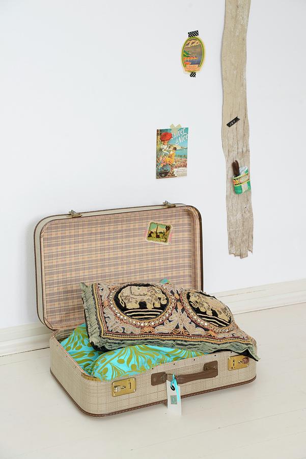 Scatter Cushions In Open Vintage Suitcase Next To Wooden Board On Wall Photograph by Revier 51