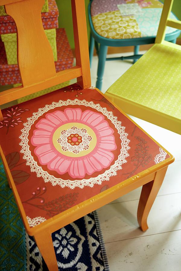 Seat Of Orange-painted Wooden Chair Painted With Pink And Red Floral Motif In Front Of Further Colourful Chairs Photograph by Tine Guth Linse