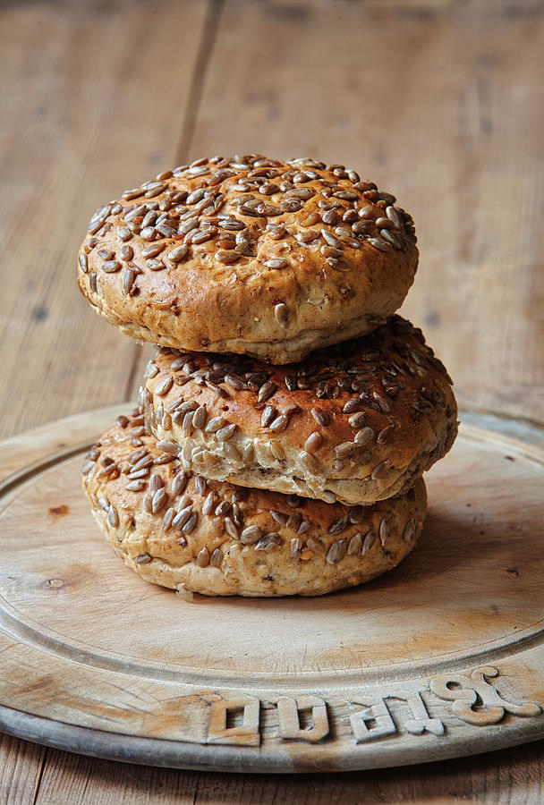Seeded Bread Rolls Stacked On An Antique Bread Board Photograph by David Milnes