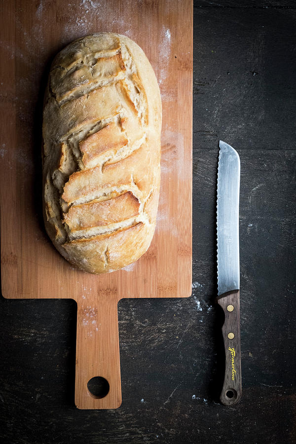 Selfmade Bread On A Wooden Planl With A Bread Knife And A Dark Backdrop Photograph by Lucie Beck