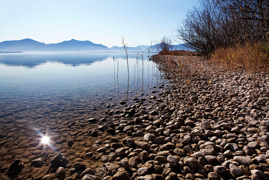 Shallow Water Beside A Gravel Bank In Lake Chiemsee And The Chiemgau Mountains In The Background Photograph by Wolfgang Gasser