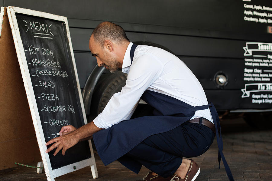 Transportation Photograph - Side View Of Male Vendor Writing On Blackboard While Crouching At Street By Food Truck by Cavan Images