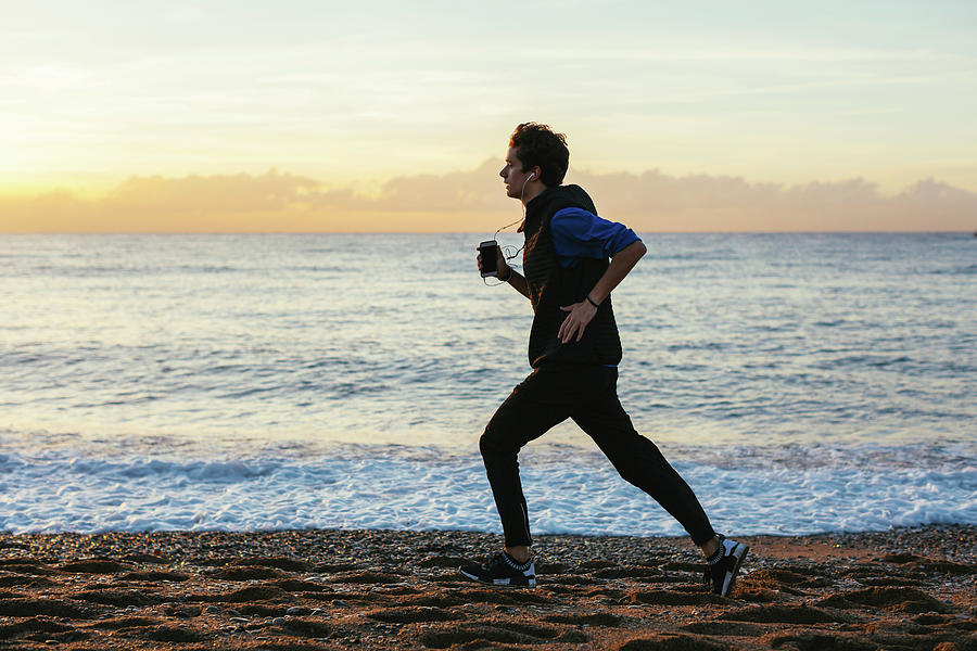 Side View Of Teenage Boy Listening Music While Jogging At Beach Against ...