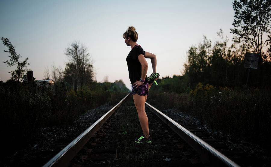 Nature Photograph - Side View Of Woman Stretching Leg While Standing On Railroad Track Against Sky During Dusk by Cavan Images
