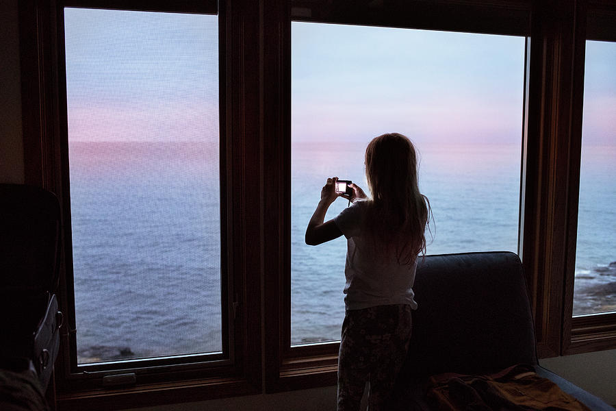 Girl Photograph - Silhouette Girl Photographing Sea Through Window While Standing In Log Cabin by Cavan Images