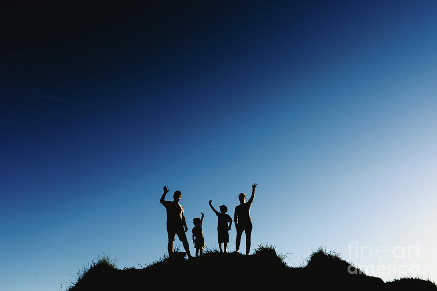 Silhouette of a happy family on top of a hill waving at sunset. Photograph by Joaquin Corbalan