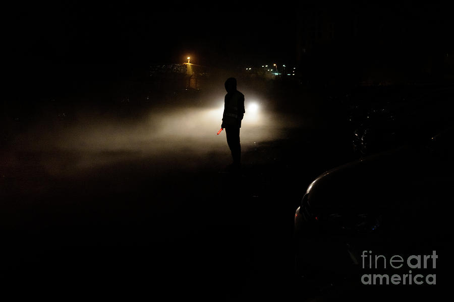 Silhouette of unrecognizable man illuminated by the headlights of a car on a dark night. Photograph by Joaquin Corbalan
